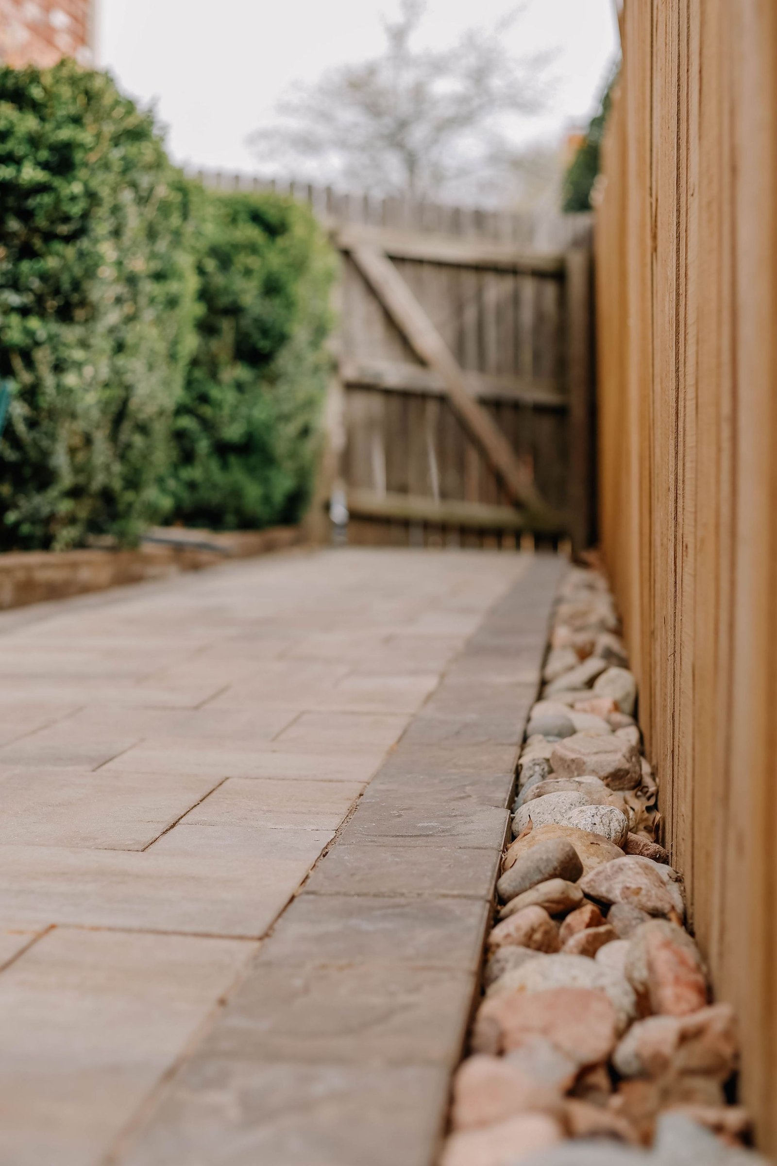 Paver walkway with river-stone border along a wooden fence