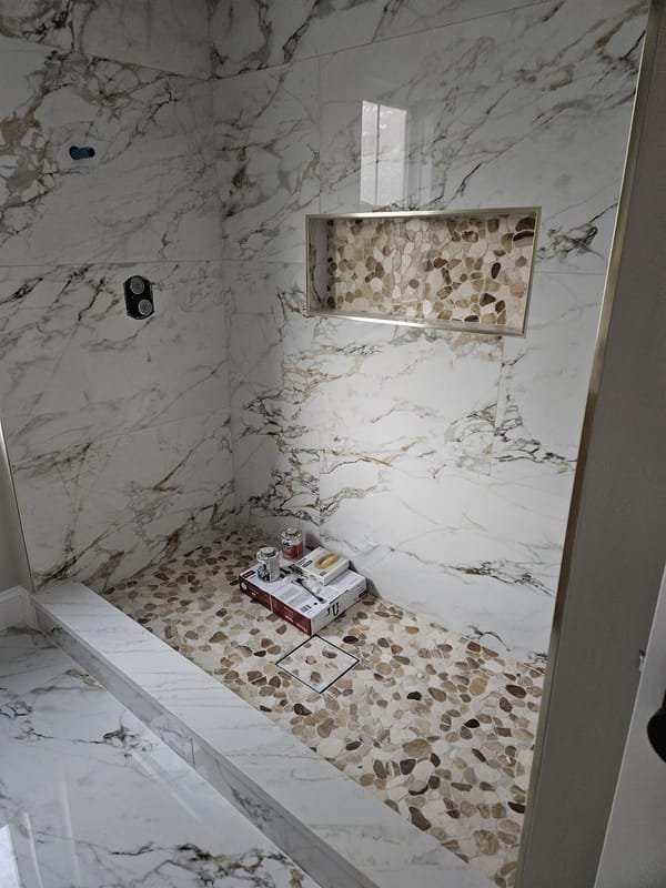 Marble-look porcelain shower with a gold niche and pebble floor