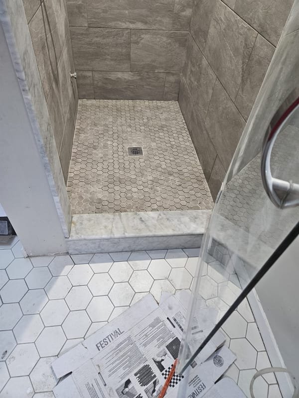 Gray tile shower with a tan hexagon floor